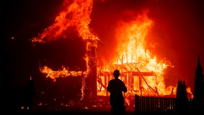 In this Nov. 8, 2018 file photo, a home burns as a wildfire called the Camp Fire rages through Paradise, Calif. Pacific Gas and Electric says it has reached a $13.5 billion settlement that will resolve all major claims related to devastating wildfires blamed on its outdated equipment and negligence. The settlement, which the utility says was reached Friday, Dec. 6, 2019, still requires court approval.