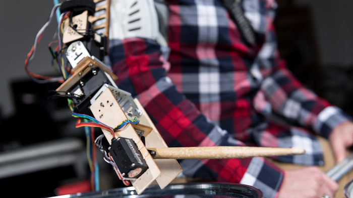 The robotic arm attaches to a drummer's right shoulder and plays the cymbal and tom.