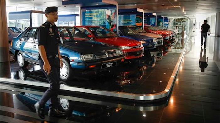 A Malaysian policeman walks by a fleet of national cars on display at the Proton Centre of Excellence Complex in Kuala Lumpur, Malaysia, Tuesday, March 1, 2016. Malaysian national car company Proton says it has begun shipping left-hand drive sedans to Chile as it seeks to tap new markets and revitalize exports.