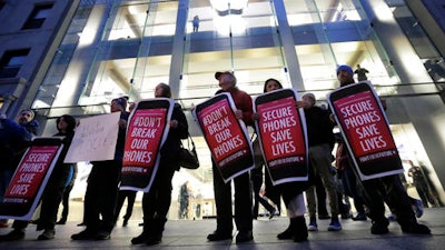 In this Tuesday, Feb. 23, 2016, file photo, protesters carry placards outside an Apple store in Boston. Tech companies, security experts and civil liberties groups are filing court briefs supporting Apple in its battle with the FBI. The groups oppose a judge’s order that would require Apple to help federal agents hack an encrypted iPhone used by a San Bernardino mass shooter.