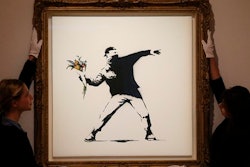 In this Monday, June 24, 2013 file photo, Bonhams employees adjust a spray paint work by urban artist Banksy at Bonhams auction house in London.