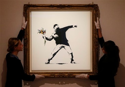 In this Monday, June 24, 2013 file photo, Bonhams employees adjust a spray paint work by urban artist Banksy at Bonhams auction house in London.