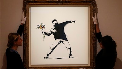 In this Monday, June 24, 2013 file photo, Bonhams employees adjust a spray paint work by urban artist Banksy at Bonhams auction house in London.