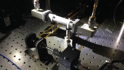 Measurements of electrical properties of a plastic tape (yellow), taken using a specially designed microwave cavity (the white cylinder at center) and accompanying electrical circuit, change quickly and consistently in response to changes in the tape's thickness. The setup is inspired by high-volume roll-to-roll manufacturing devices used to mass-produce nanomaterials. The changes in the tape's thickness spell NIST in Morse code.