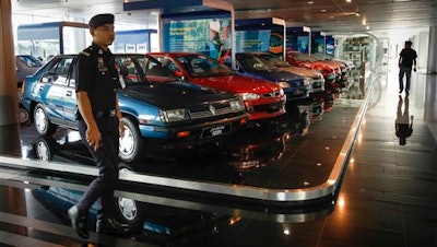 A Malaysian policeman walks by a fleet of national cars on display at the Proton Centre of Excellence Complex in Kuala Lumpur, Malaysia, Tuesday, March 1, 2016. Malaysian national car company Proton says it has begun shipping left-hand drive sedans to Chile as it seeks to tap new markets and revitalize exports.