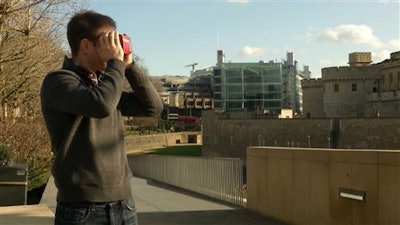 This Feb. 2, 2016 image made from video shows Timelooper co-founder Andrew Feinberg looking through a Google cardboard virtual reality headset across from the Tower of London in London, England. The Timelooper app allows users to experience key moments in London history with just a smartphone and a cardboard headset.