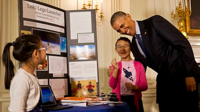 President Barack Obama laughs as he hugs Rebecca Yeung, 11, from Seattle, Wash., next to her sister Kimberly Yeung, 9, as they show him their homemade “spacecraft” that features a photograph of their late cat and is made of archery arrows and wood scraps which they launched into the stratosphere via a helium balloon that records location coordinates, temperature, velocity, and pressure and reports the data back to the them, Wednesday, April 13, 2016, during the 2016 White House Science Fair at the White House in Washington.