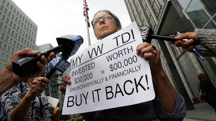 Joyce Ertel Hulbert, owner of a 2015 Volkswagen Golf TDI, holds a sign while interviewed outside of the Phillip Burton Federal Building in San Francisco, Thursday, April 21, 2016. An agreement will give consumers who bought nearly 600,000 Volkswagen vehicles rigged to cheat on emissions tests the option of having the automaker buy back the cars or fix them, a judge said Thursday.