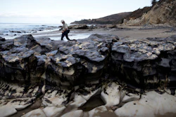 In this file photo, David Ledig, a national monument manager from the Bureau of Land Management, walks past rocks covered in oil at Refugio State Beach, north of Goleta, CA.