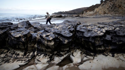 In this file photo, David Ledig, a national monument manager from the Bureau of Land Management, walks past rocks covered in oil at Refugio State Beach, north of Goleta, CA.
