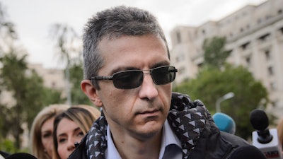 In this May 10, 2016 picture Dan Condrea, the head of pharmaceutical company Hexi Pharma walks surrounded by media to the prosecutor's office in Bucharest, Romania. A person who was killed when a car slammed into a tree Sunday, May 22, 2016, hasn’t been identified but police say they found identity documents in the car belonging to the CEO of the pharmaceutical company Hexi Pharma.