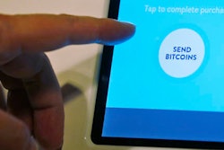 In this Thursday, March 13, 2014, file photo, Ken Lo, CEO of ANXBTC Bitcoin Exchange, points to the screen of his Bitcoin ATM during a demonstration in Hong Kong. For years, the question of who created bitcoin has been one of the biggest parlor games in some corners of cryptography and computer science.