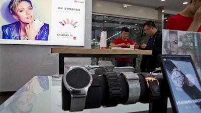 In this Friday, May 13, 2016 photo, a sales person attends to a customer at a Huawei retails shop with an advertisement for the P9 featuring Scarlett Johansson in Beijing, China. This year, its 6-year-old consumer brand launched a new flagship, the P9, and is positioning it to compete with Apple and Samsung.