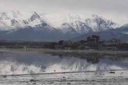 In this Feb. 12, 2016, file photo, the Chugach Mountains and the buildings of downtown Anchorage, Alaska, are reflected in the still waters of Cook Inlet. A national environmental group, the Center for Biological Diversity, has asked the National Marine Fisheries Service to block plans in Cook Inlet by an oil company for hydraulic fracturing, the extraction of oil and gas from rock by injecting high-pressure mixtures of water, sand or gravel and chemicals, because of possible harmful effects on endangered belugas.