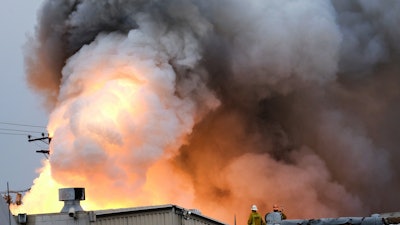 Los Angeles County Firefighters stand on top of a roof and watch as an explosion erupts from a factory in Maywood, Calif. on Tuesday, June 14, 2016. Explosions rocked a small Los Angeles County city early Tuesday as an inferno raged through a business containing metals and and firefighters decided to allow the blaze to burn itself out.