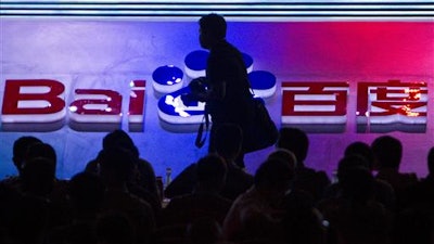 In this Sept. 2, 2011 file photo, a photographer walks past the logo of Baidu Inc., which operates China's dominant search engine, during a technology innovation conference held by the company at China's National Convention Center in Beijing, China. China issued new regulations on Saturday, June 25, 2016 demanding search engines clearly identify paid search results, months after a terminally-ill cancer patient complained that he was misled by the giant search engine Baidu.