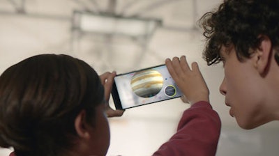 This image provided by Google shows people looking at a view of the solar system using technology Google calls 'Project Tango.' Tango uses software and sensors to track motions and size up the contours of rooms, which can empower a smartphone to map building interiors. That’s a crucial building block of a promising new frontier in “augmented reality,” or the digital projection of lifelike images and data into a real-life environment.