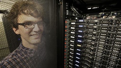 In this Wednesday, June 22, 2016, photo, Massachusetts Institute of Technology researcher Carl Vondrick looks through a protective door while standing next to a computer server cluster, right, on the MIT campus, in Cambridge, Mass. MIT says a computer that binge-watched TV shows such as “The Office,” “Big Bang Theory” and “Desperate Housewives” learned how to predict whether the actors were about to hug, kiss, shake hands or slap high-fives, a breakthrough that eventually could help the next generation of artificial intelligence function less clumsily.