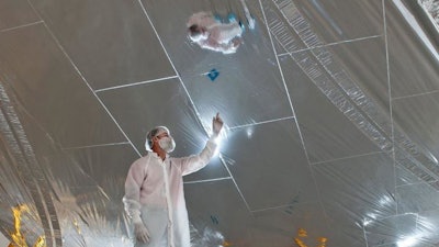 An engineer in a cleanroom looks at one of the sunshield layers that shows a grid pattern of 'rip-stops.'