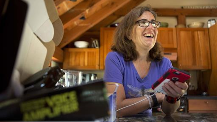In this Friday, June 24, 2016, photo, Jessie Levine smiles as she listens to her recorded outgoing phone message on her iPhone in Springfield, N.H. Levine was diagnosed with Lou Gehrig's disease or ALS in 2015, and it has caused her speech to become slow and slurred. She is now exploring a new way to restore her voice via speech synthesis, or the artificial production of human speech.