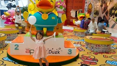 A child poses for photos near a display of merchandise at a shopping mall in Beijing, China. China's economic growth held steady in the most recent quarter, according to official data released Friday, indicating policies meant to counter the slowdown in the world's second biggest economy are paying off for the moment.