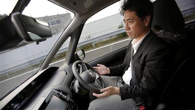In this July 12, 2016 photo, Nissan Motor Co. Deputy General Manager Atsushi Iwaki gets his hands off of the steering wheel of a self-driving new Serena minivan during a test drive at Nissan test course in Yokosuka, near Tokyo. The Serena minivan equipped with ProPilot technology relies on a single camera in the back of the driver's rearview mirror. The car can then follow the vehicle ahead, maintaining a safe distance that the driver sets.