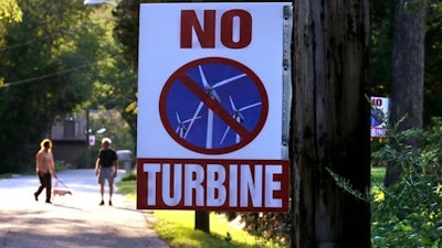 In this Thursday, Aug. 25, 2016 photo, a sign against a proposed wind turbine hangs from a neighborhood telephone pole, in North Smithfield, R.I. Even as Rhode Island makes history as the first U.S. state with an offshore wind farm, its people are not so fond of wind turbines sprouting up on land near where they live. Town leaders in North Smithfield are proposing a ban on any new wind turbines in the rural community near the Massachusetts border.