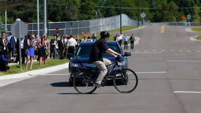 In this July 20, 2015 file photo, a cyclist crosses in front of a vehicle as part of a demonstration at Mcity on the University of Michigan campus in Ann Arbor, Mich. Automakers say cars that wirelessly talk to each other are finally ready for the road. The cars hold the potential to dramatically reduce traffic deaths, improve the safety of self-driving cars and someday maybe even help solve traffic jams. Government and industry have spent more than a decade and more than $1 billion researching and testing the technology, known as vehicle-to-vehicle communications, or V2V.