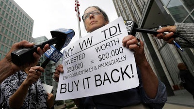 In this Thursday, April 21, 2016, file photo, Joyce Ertel Hulbert, owner of a 2015 Volkswagen Golf TDI, holds a sign while interviewed outside of the Phillip Burton Federal Building in San Francisco.