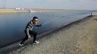 In this Feb. 25, 2016, file photo, Sha Xinog, climbs the bank to get more bait while fishing along the California Aquaduct near Firebaugh, Calif. Critics and a California lawmaker want more answers from Gov. Jerry Brown's administration on who's paying for a proposed giant water project. That's after a Southern California water district said Thursday, Aug. 11, 2016, that Brown's administration is now stating that state or federal funds will be used to finish planning for two $16 billion water tunnels.