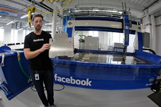 In this photo taken Tuesday, Aug. 2, 2016, model maker Spencer Burns, holds up a piece of sheet metal while standing in front of a water jet during a tour of Area 404, the hardware R&D lab, at Facebook headquarters in Menlo Park, Calif.