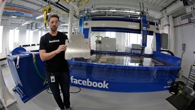 In this photo taken Tuesday, Aug. 2, 2016, model maker Spencer Burns, holds up a piece of sheet metal while standing in front of a water jet during a tour of Area 404, the hardware R&D lab, at Facebook headquarters in Menlo Park, Calif.