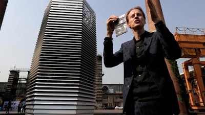 Dutch artist Daan Roosegaarde holds a packet containing smog particles collected by the Smog Free Tower as he presents his machine at D-751art district in Beijing, Thursday, Sept. 29, 2016. In a city where smog routinely blankets the streets and chokes off clean air, a Dutch artist has offered an eccentric solution: a 20-foot metal tower that takes in smog and purifies it like a giant outdoor vacuum cleaner.