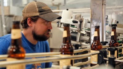 In this Tuesday, Sept. 6, 2016 photo, Jordan Wambeke, head brewer of the Carakale Brewery in Fuheis, Jordan, keeps an eye on the labeler machine in the brewery's bottling assembly line. The Jordanian microbrew is starting to export to the United States its signature blonde, Indian pale ale, and a coffee porter dosed with roasted cardamom.