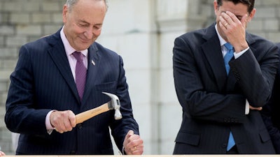House Speaker Paul Ryan of Wis., right, hides his face and laughs at Sen. Charles Schumer, D-N.Y., bends his nail during a ceremony to drive in the first nails to signifying the start of construction on the 2017 presidential inaugural platform, Wednesday, Sept. 21, 2016, on Capitol Hill in Washington.
