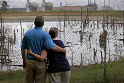 In this April 25, 2014, file photo, Bryant Gobble, left, embraces his wife, Sherry Gobble, right, as they look from their yard across an ash pond full of dead trees toward Duke Energy's Buck Steam Station in Dukeville, N.C. Duke Energy has agreed to remove millions of tons of coal ash containing toxic heavy metals from a power plant in North Carolina. The nation’s largest electricity company announced Wednesday, Oct. 5, 2016 that it would dig up three huge pits of water-logged ash at the Buck Steam Station near Salisbury. The ash will be dried and either offered for use in making concrete or moved to lined landfills elsewhere.