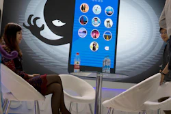 In this file photo, a woman sits near a display showing the dangers of hackers breaking into mobile devices during the Global Mobile Internet Conference in Beijing. Chinese electronics maker Hangzhou Xiongmai Technology has issued a recall for millions of products sold in the U.S. following a devastating cyberattack, but has lashed out at critics who say its devices were at fault.