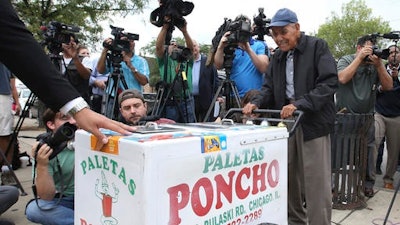 In this photo taken Sept. 21, 2016, a grateful Fidencio Sanchez pushes his paletas cart one last time before a group of of media after accepting a check for $384,290 during a news conference outside the ice cream shop, Paleteria y Neveria Poncho, where he rented his paletas cart in Chicago's Little Village.