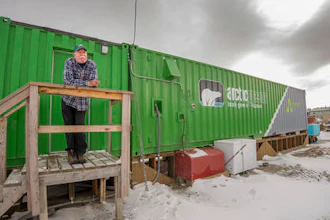 In this Oct. 26, 2016 photo provided by Will Anderson, employee Joe Carr stands outside a new indoor hydroponics farm owned by a local Alaska Native corporation in Kotzebue, Alaska. Arctic Greens is harvesting kale, various lettuces, basil and other greens weekly from the soil-free system and selling them at the supermarket in the community of nearly 3,300.