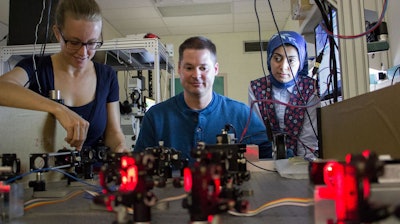 UNM Associate Professor Keith Lidke (center) is working at an optics table with post-doctoral student Marjolein Meddens (l.) and graduate student Hanieh Mazloom-Farsibaf (r.).