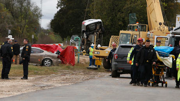 A victim, right, from one of two automobiles, background, is taken away after the cars fell into a sinkhole in San Antonio, Texas, Monday, Dec. 5, 2016.