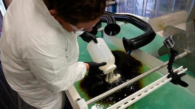 PNNL microbiologist Robert Jeters sprinkles PNNL's chemically modified sawdust onto a small oil spill inside the Arctic simulation lab, where researchers mimic extreme freezing conditions and make icy slush that is similar to what is found on the surface of the Arctic Sea.