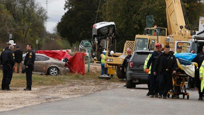 A victim, right, from one of two automobiles, background, is taken away after the cars fell into a sinkhole in San Antonio, Texas, Monday, Dec. 5, 2016.