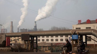 A man rides a bike past smoke spewing from the sprawling complex that is a part of the Jiujiang steel and rolling mills in Qianan in northern China's Hebei province. China's top economic planner pledged Tuesday, Jan 10, 2017, to continue cutting steel and coal production that have been a source of trade friction with many countries.