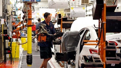 In this April 6, 2016, photograph, Nissan technician David Newton uses a lift to move a front seat for installation into a new Altima on the assembly line at the Nissan Canton Vehicle Assembly Plant in Canton, Miss. U.S. businesses ramped up their investment in industrial machinery, semiconductors, and other big-ticket items in December 2016, boosting demand for factory goods. Auto sales reached a record level in 2016, and automakers continued cranking out vehicles through the end of the year.