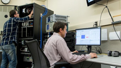 Rick Candell (seated) and Murat Aksu (standing) examine how wireless communications perform in a virtual chemical processing plant created by the NIST Industrial Wireless Test Bed. Data collected from a recent study of wireless propagation in three real factory settings will enhance the ability of the test bed to accurately simulate a variety of industrial environments.