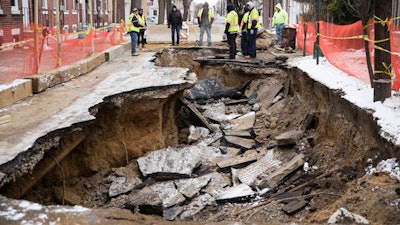 Workers inspect a sinkhole in Philadelphia, Monday, Jan. 9, 2017. The Philadelphia Water Department said a water main break caused the sinkhole to open up on the street.