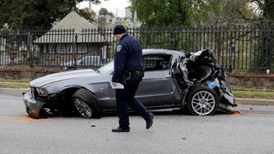In this Nov. 1, 2016 file photo, a member of the Baltimore Police Department walks past a car that was damaged by a school bus before the bus was involved in a fatal collision with a commuter bus in Baltimore. A jump in traffic fatalities last year pushed deaths on U.S. roads to their highest level in nearly a decade, erasing improvements made during the Great Recession and economic recovery, a leading safety organization said Wednesday, Feb. 15, 2015.