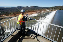 In this Saturday, Feb. 11, 2017, photo, Jason Newton, of the Department of Water Resources, takes a picture of water going over the emergency spillway at Oroville Dam in Oroville, Calif. Officials have ordered residents near the Oroville Dam in Northern California to evacuate the area Sunday, Feb. 12, saying a 'hazardous situation is developing' after an emergency spillway severely eroded.