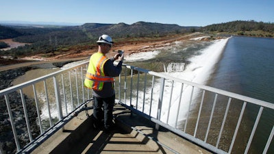 In this Saturday, Feb. 11, 2017, photo, Jason Newton, of the Department of Water Resources, takes a picture of water going over the emergency spillway at Oroville Dam in Oroville, Calif. Officials have ordered residents near the Oroville Dam in Northern California to evacuate the area Sunday, Feb. 12, saying a 'hazardous situation is developing' after an emergency spillway severely eroded.